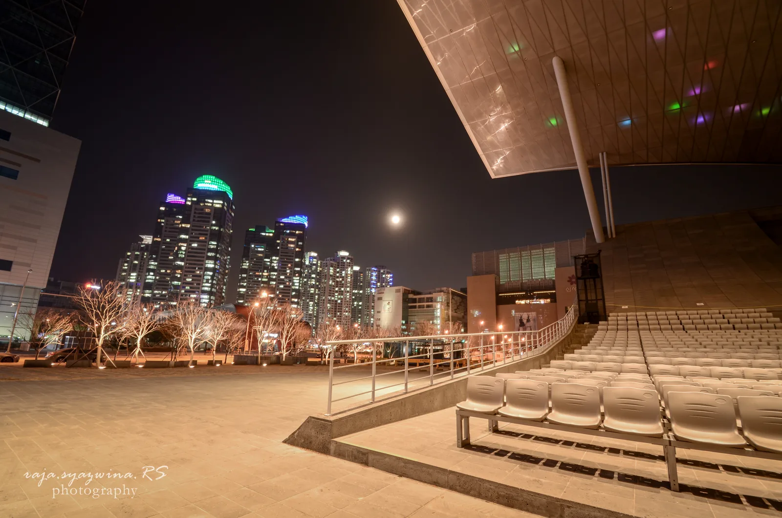 Cobertura iluminada do Centro de Cinema de Busan diante dos edifícios de Centum City à noite