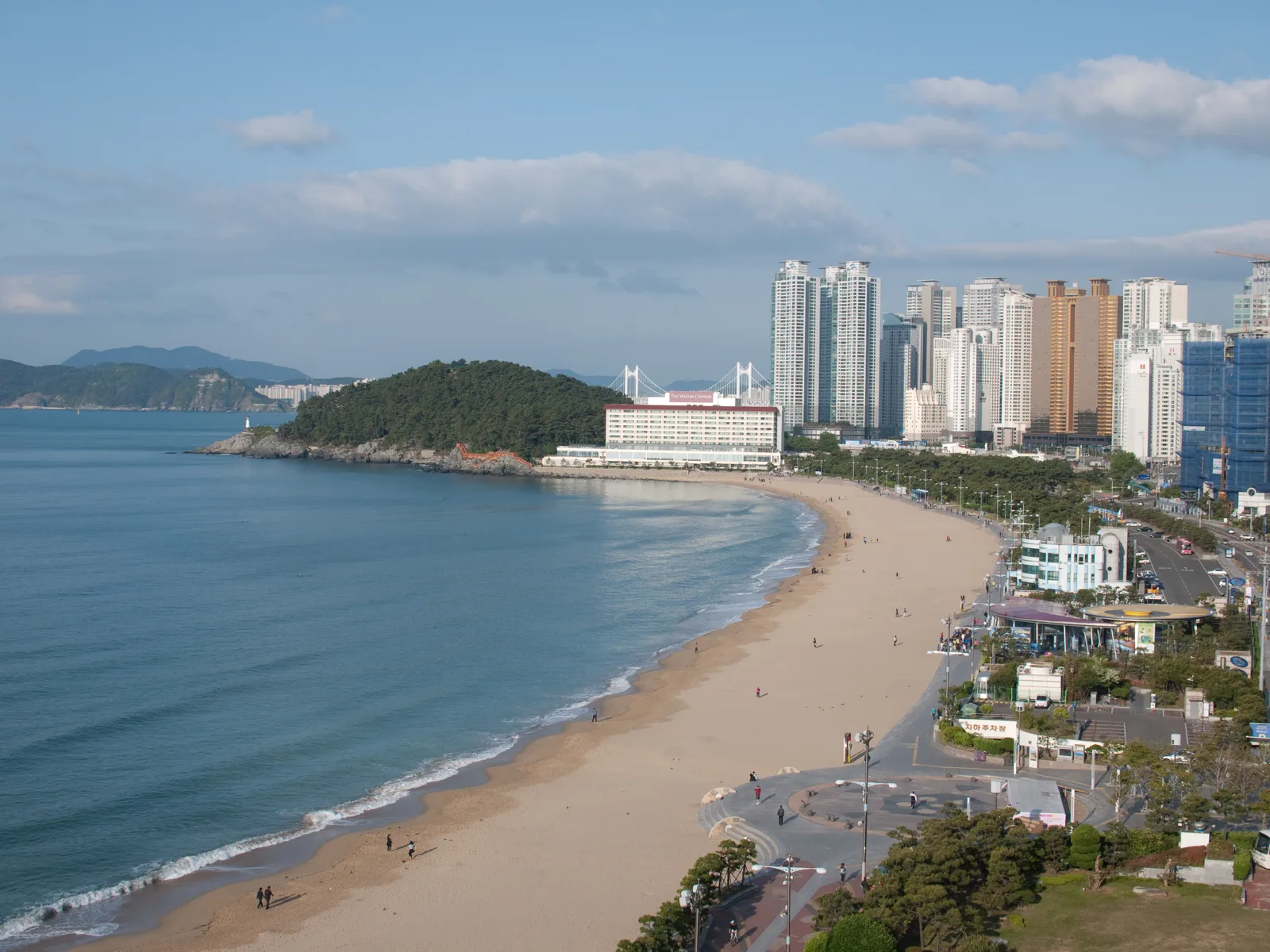 Praia de Haeundae com mar, areia, edifícios e a área arborizada de Dongbaek, em fotografia de 2009.