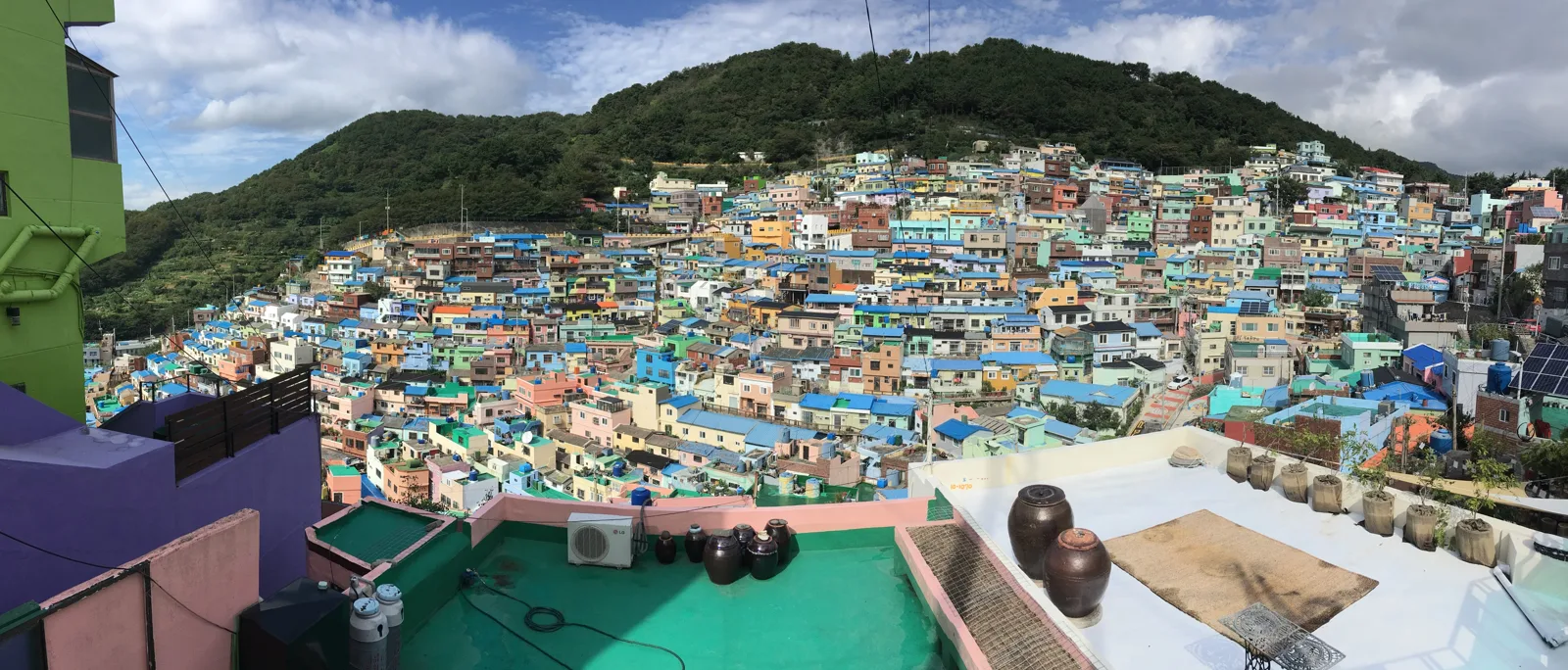 Panorama das casas coloridas de Gamcheon ocupando as encostas, com a cidade e o mar ao fundo.